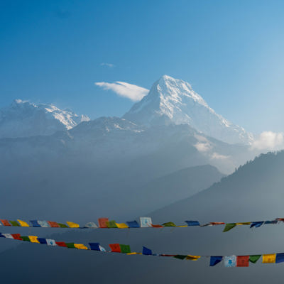 Nepalese vlag en gebedsvlaggetjes met besneeuwde Himalaya-berg op de achtergrond tijdens 22-35ers reis Nepal.
