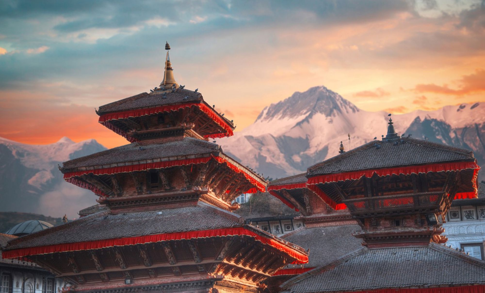 Nepalese tempel met pagodedaken bij zonsondergang, met besneeuwde Himalaya-bergen op de achtergrond.