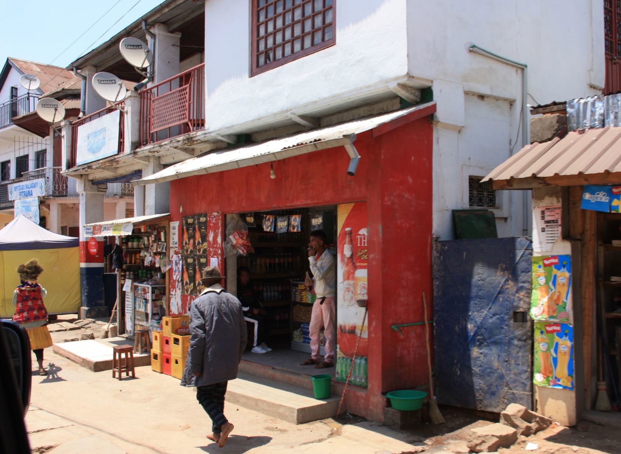 Straatbeeld in Madagascar met kleine winkel in rood pand en bewoners op de stoep.