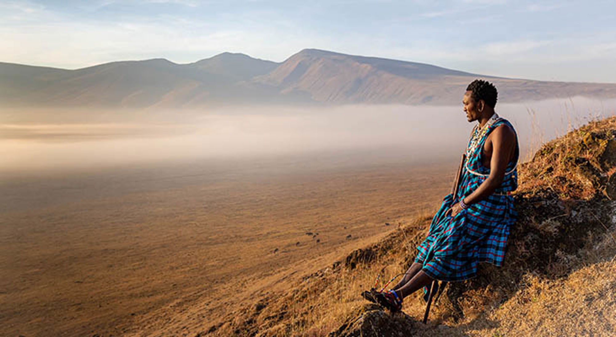 Jonge Masai krijger zittend in de krater van Ngorongoro park kijkend naar zonsopgang Jonge Masai krijger zittend in de krater van Ngorongoro park kijkend naar zonsopgang