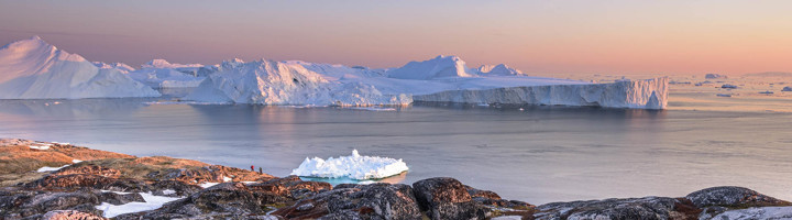 IJsbergen in een kalme fjord bij zonsondergang, gezien vanaf rotsachtige kust.