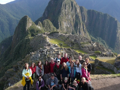 Groepsfoto van familiereis Peru bij Machu Picchu, met de Inca-ruïnes en Huayna Picchu op de achtergrond.