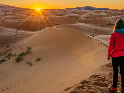 Reiziger kijkt naar zonsopkomst boven de zandduinen van de Sahara in Marokko.
