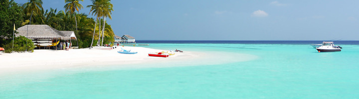 Wit zandstrand op de Malediven met palmbomen, helderblauwe lagune en bootjes.