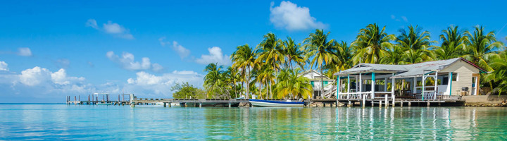 Palmbomen en strandhuisjes aan een helderblauwe lagune in Belize.