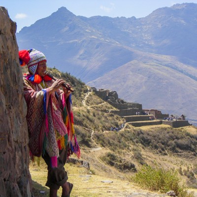 Muzikant in traditionele kleding speelt fluit bij de Inca-ruïnes van Pisac in de Heilige Vallei, Peru.
