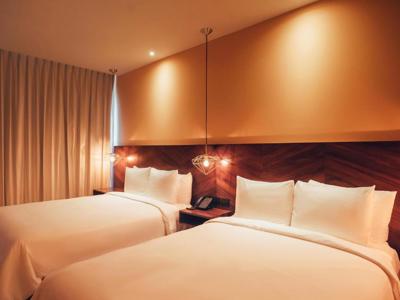 Tweepersoonskamer in Calixta hotel met twee bedden, houten hoofdbord en sfeerverlichting.