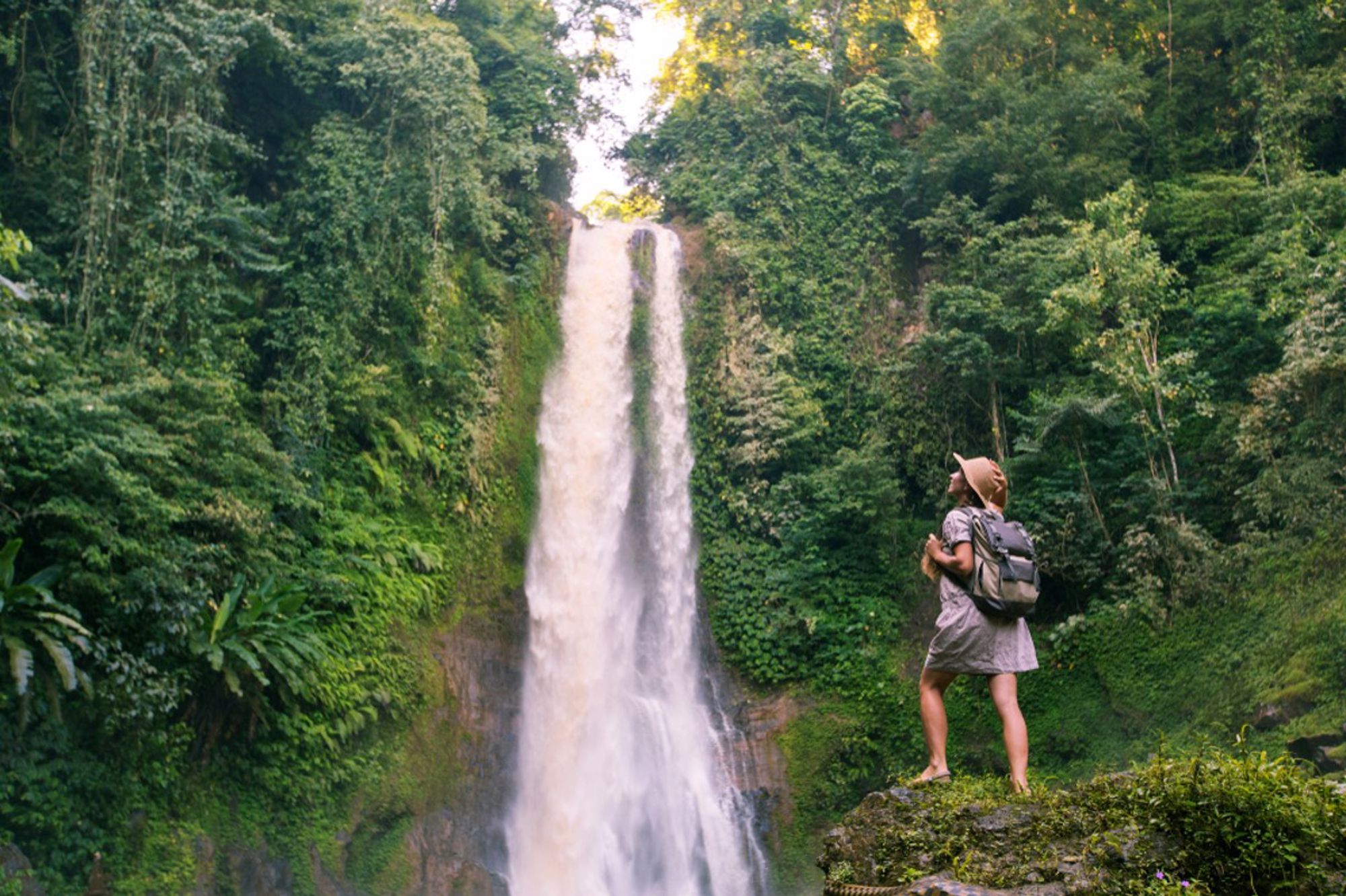 Wandelaar met rugzak bij een hoge waterval in de jungle van Indonesië.