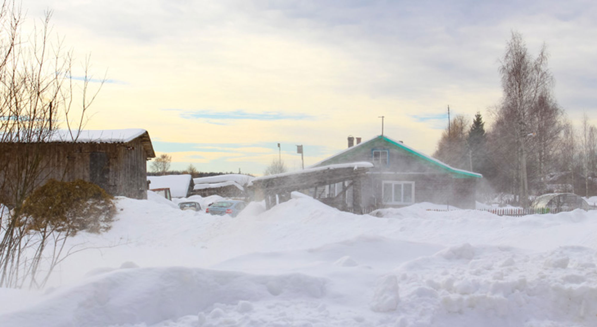 Sneeuwrijk dorp met houten huizen en opwaaiende sneeuw bij winterweer.