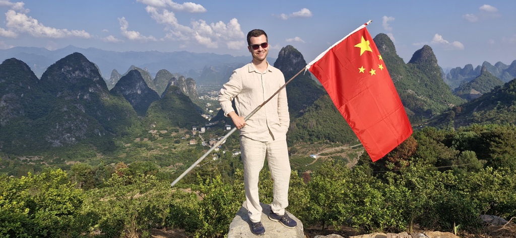 Man met Chinese vlag op uitzichtpunt met karstbergen en vallei op de achtergrond.