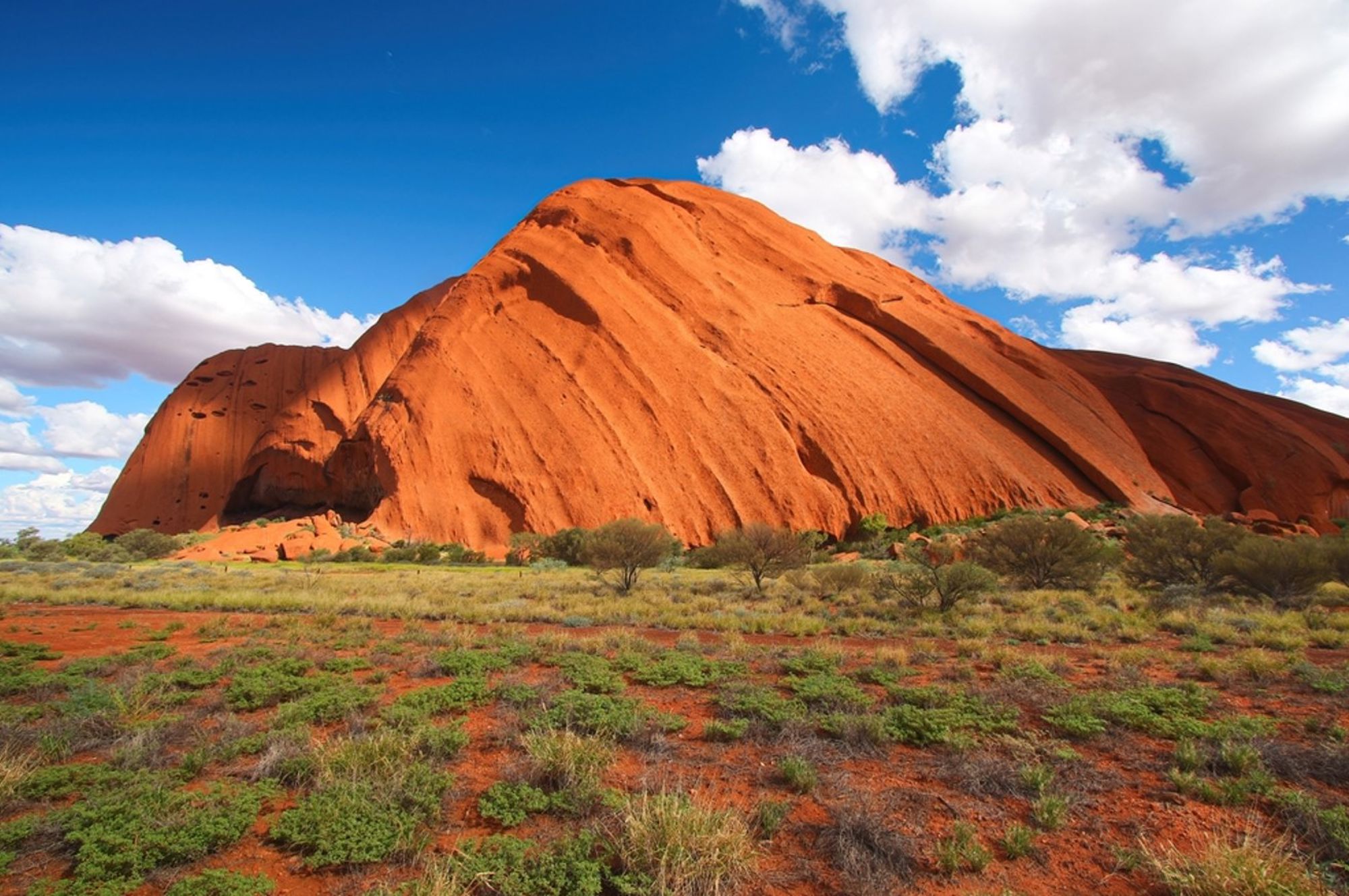Uluru (Ayers Rock) in het rode woestijnlandschap van Australië onder een blauwe lucht met wolken.