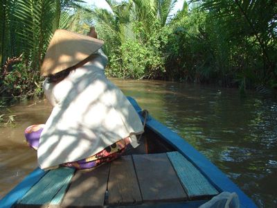 Vrouw met Vietnamese hoed in een boot op een smalle rivier tussen palmbomen in Vietnam.