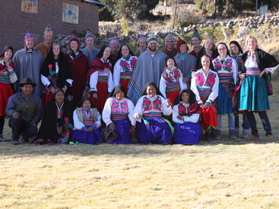Groepsfoto tijdens familiereis Peru met locals en reizigers in kleurrijke traditionele kleding in een bergdorp.
