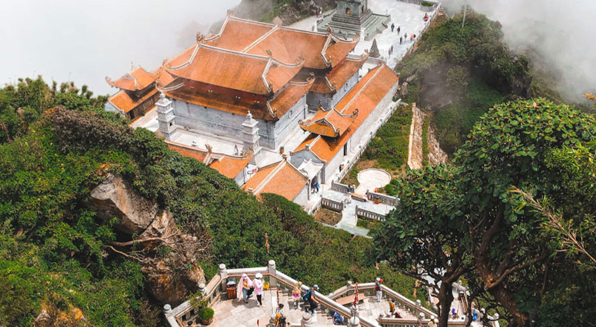 Bergtempel met oranje daken tussen groene rotsen in Vietnam, gezien vanaf een uitkijkpunt.
