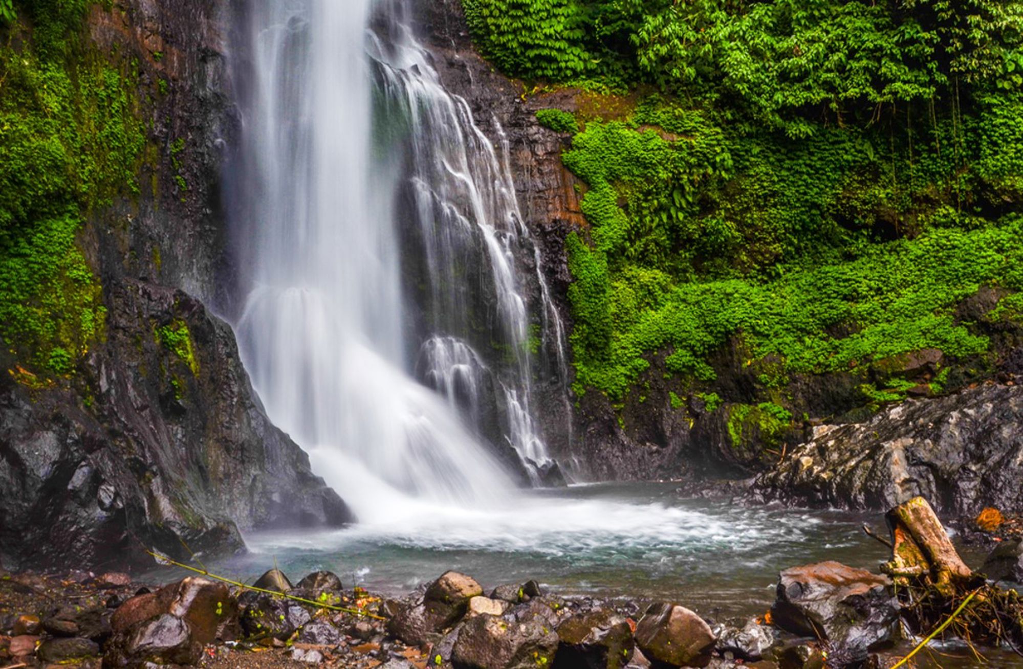 Waterval in weelderig groen regenwoud in Indonesië, met rotsen en een natuurlijke poel.