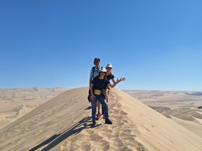 Gezin op een hoge zandduin tijdens familiereis Peru, met uitgestrekte woestijn op de achtergrond.
