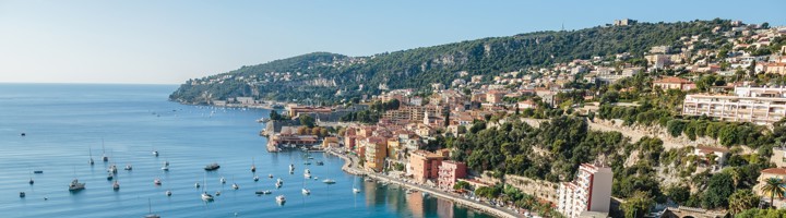 Panoramisch uitzicht op de kustplaats Villefranche-sur-Mer met azuurblauwe baai, strand en zeilboten.
