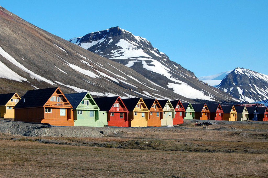 Kleurrijke houten huizen in Longyearbyen op Spitsbergen, met besneeuwde bergen op de achtergrond.