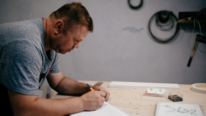 Tudor uit Moldavië werkt aan een ontwerp op papier in zijn meubelmakerij.