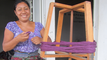Maria uit Guatemala werkt met paars garen aan een houten constructie voor het maken van textiel.