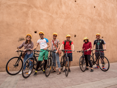 Groep fietsers met helmen poseert met fietsen voor een lemen muur tijdens een fietsvakantie in Marokko.